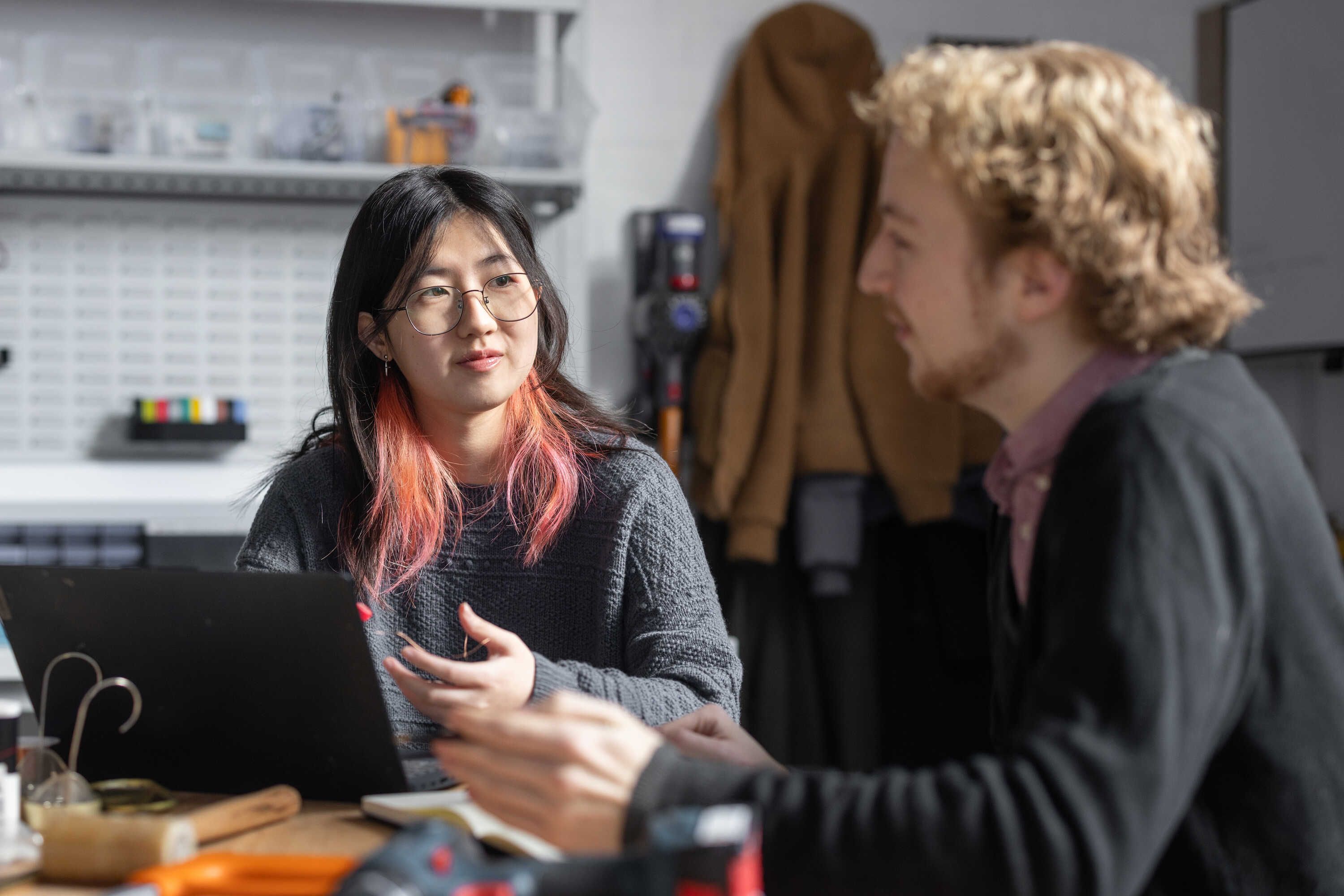 two students sitting at a desk and having a conversation in a lab