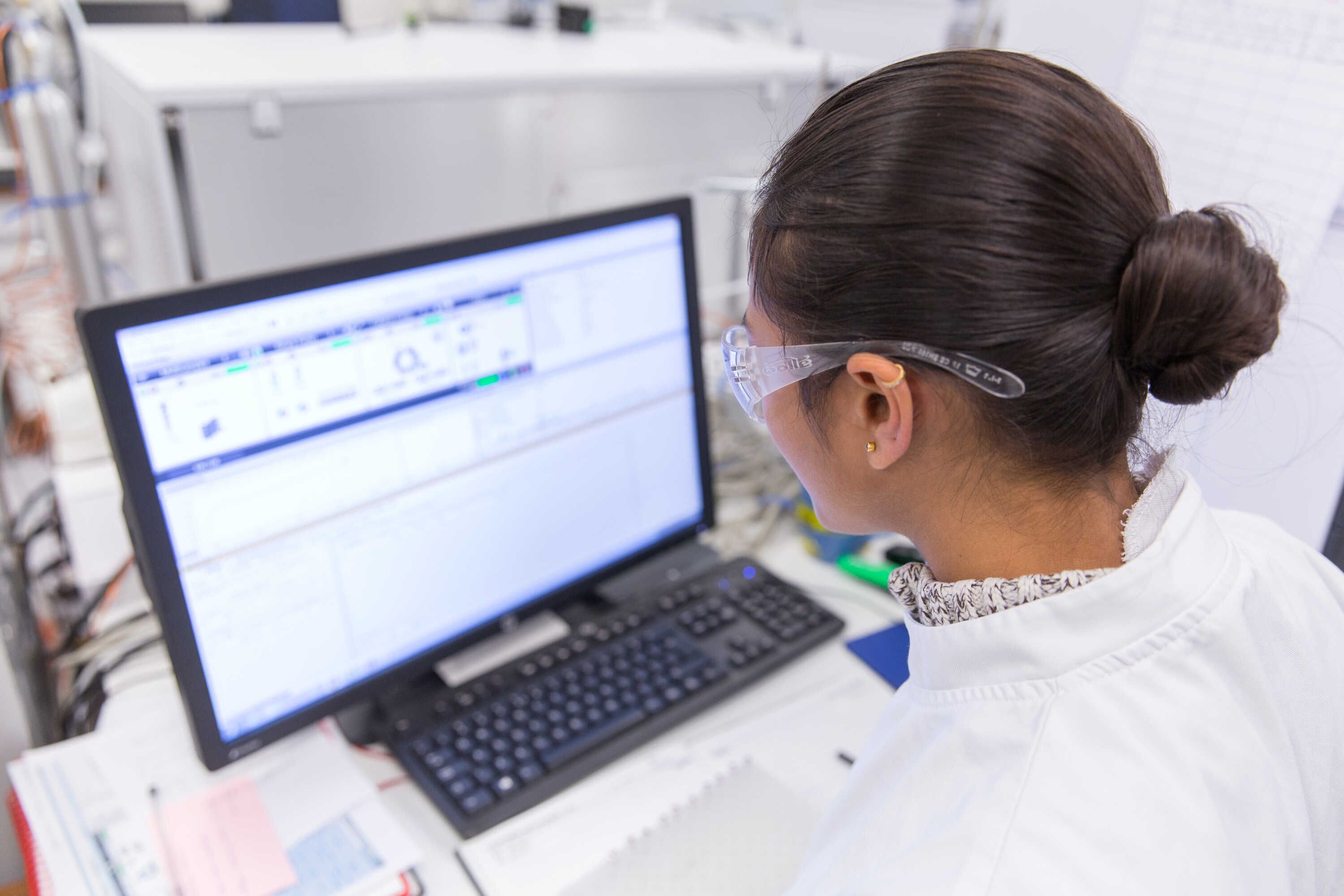 a student wearing a lab coat and transparent glasses looking at a laptop's screen