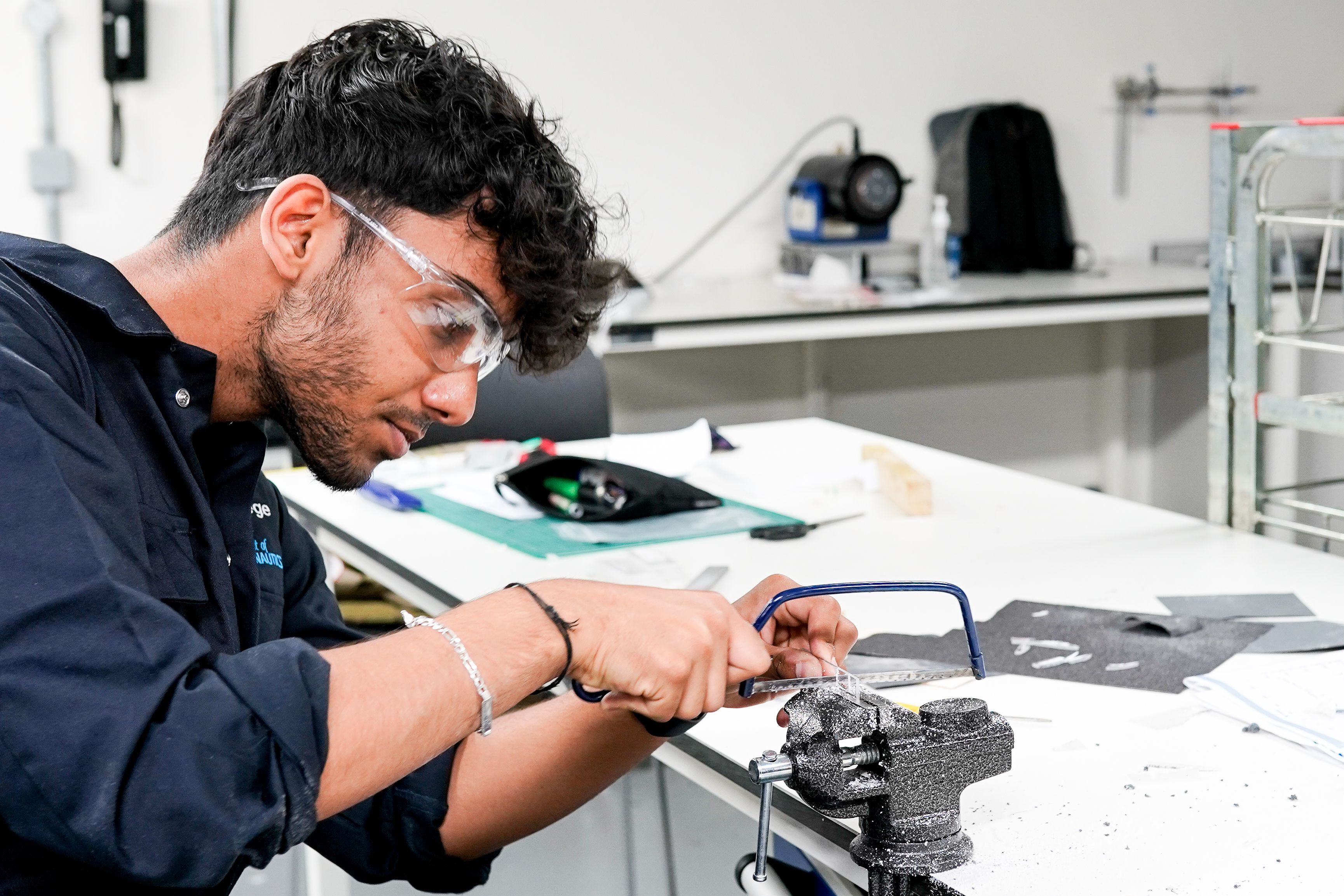 A student cutting out metal with a saw in the workshop