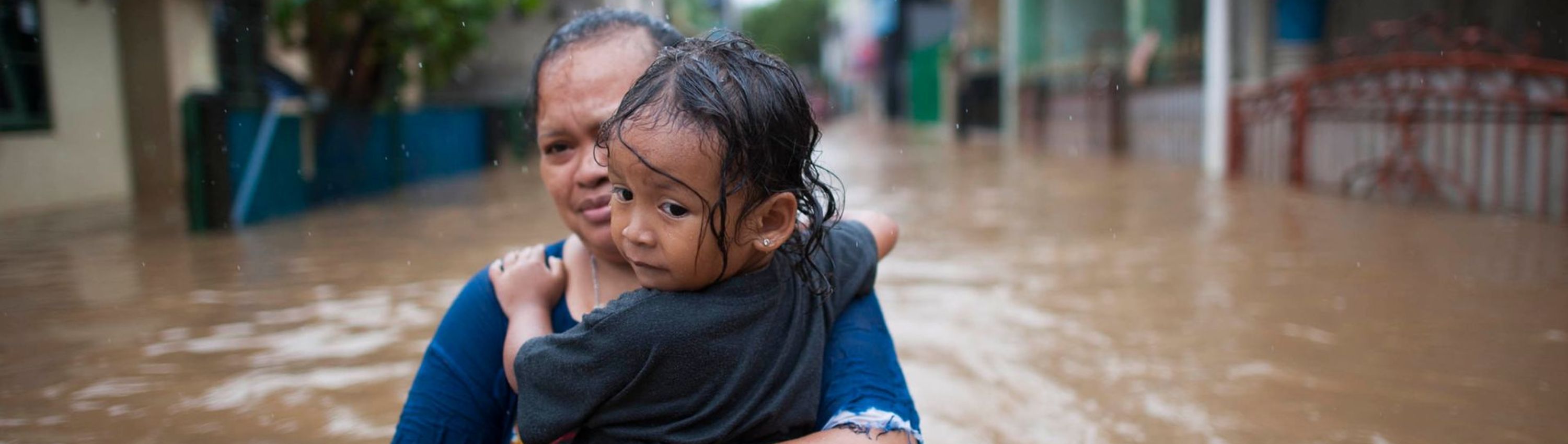 Woman and child attempting to move through a flooded village. The child is clinging to the woman.