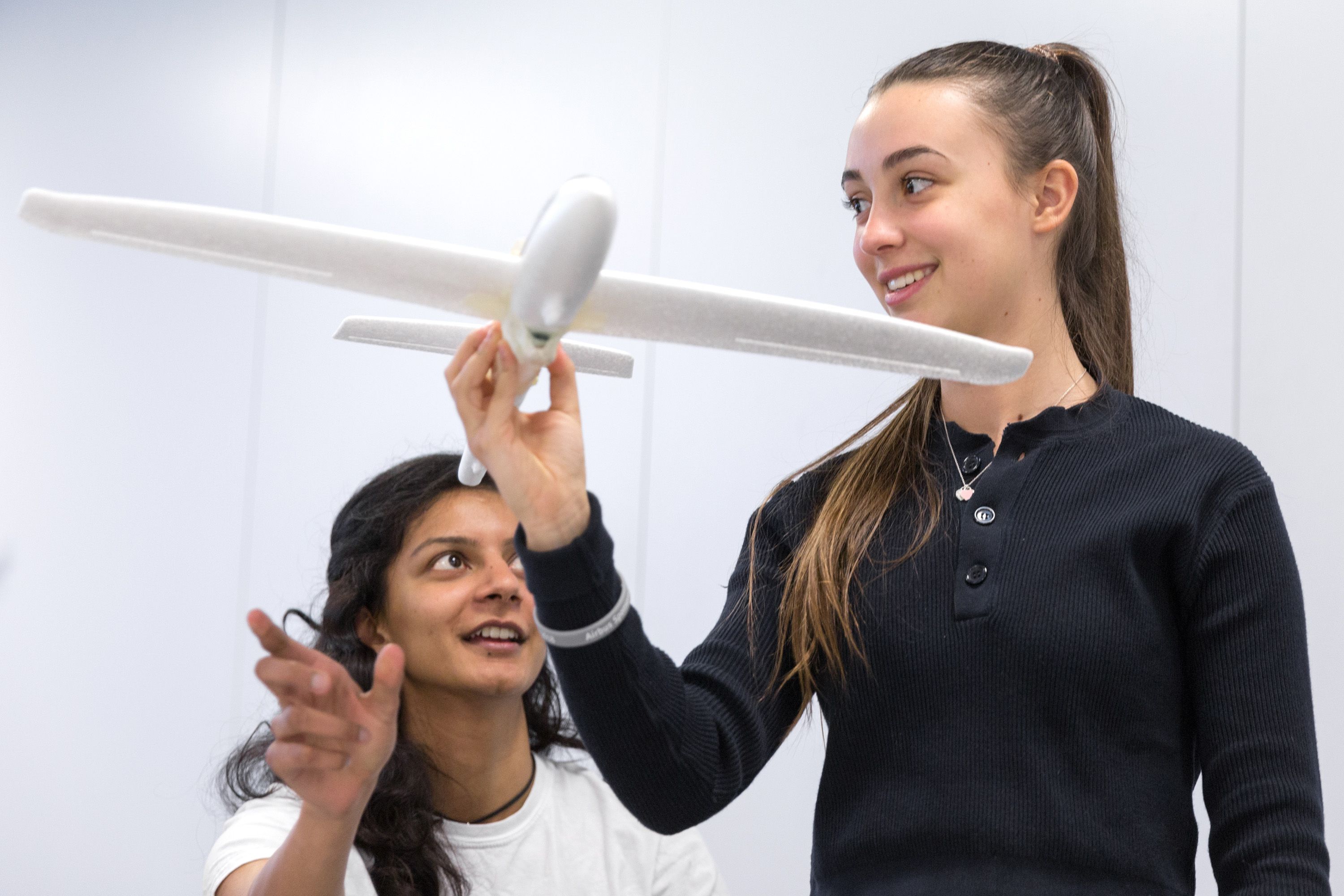 A smiling school student holds a model aeroplane while talking to a staff member