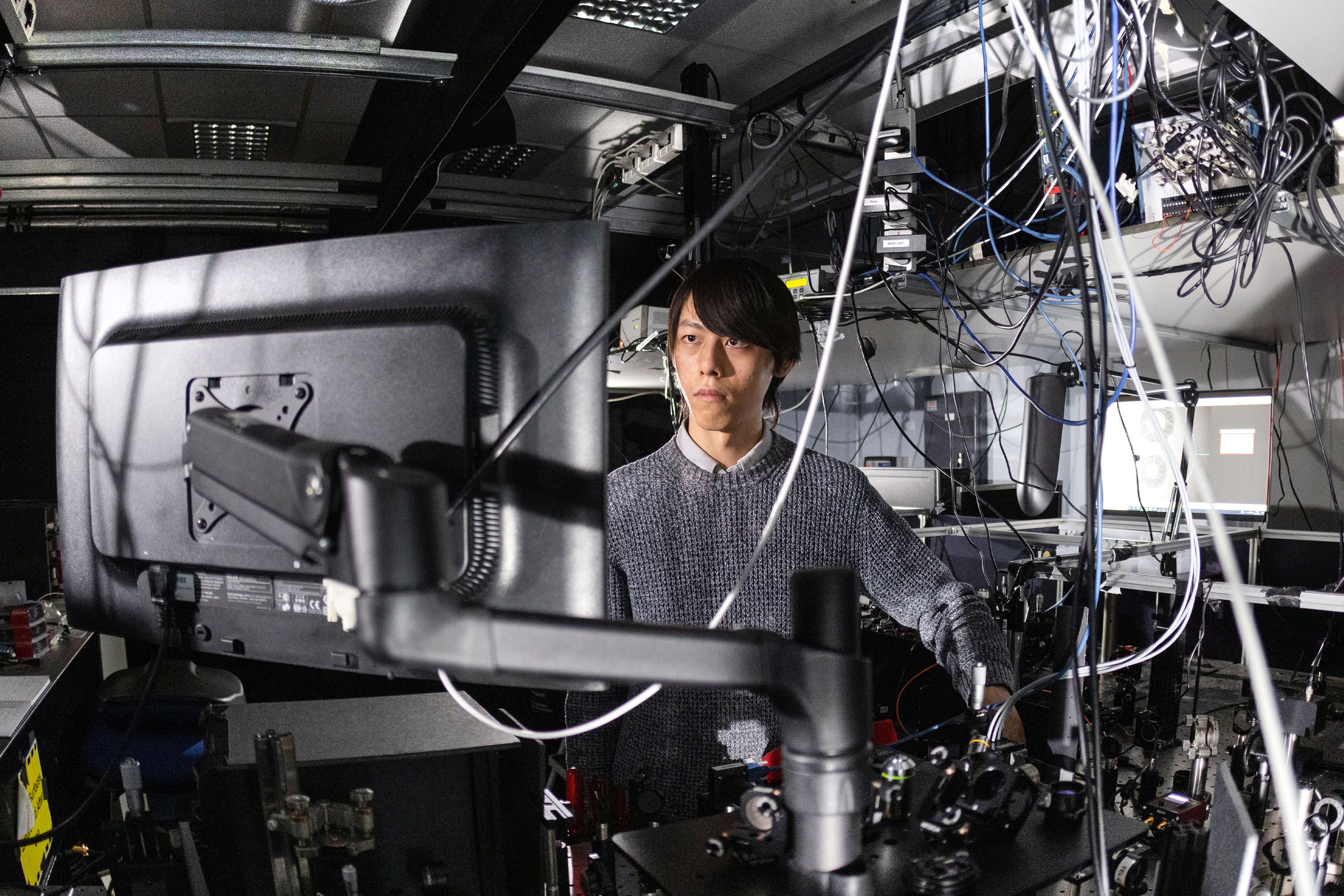 A PhD student in a lab surrounded by wires and equipment