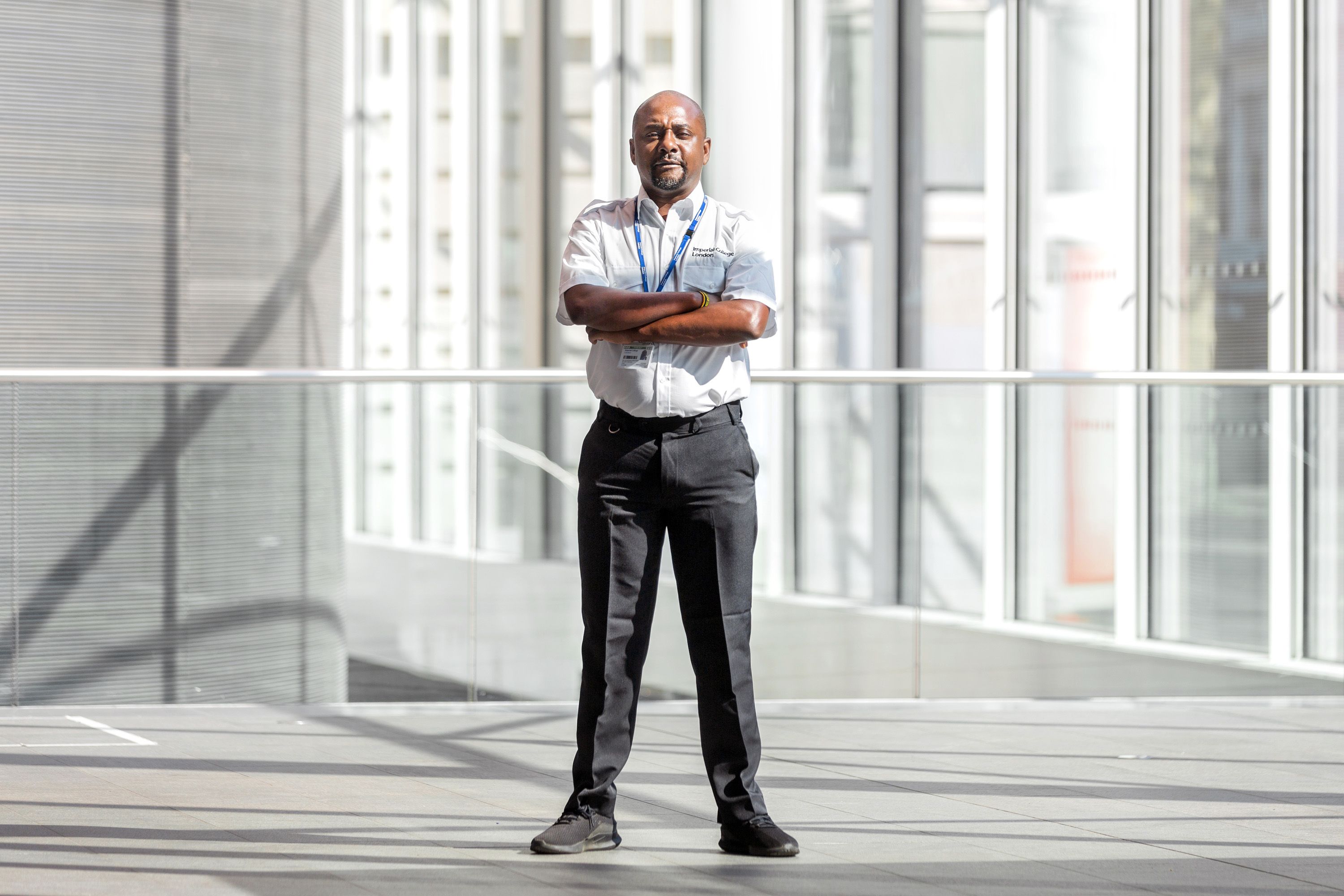 An Imperial College security guard stands in the main entrance with his arms crossed