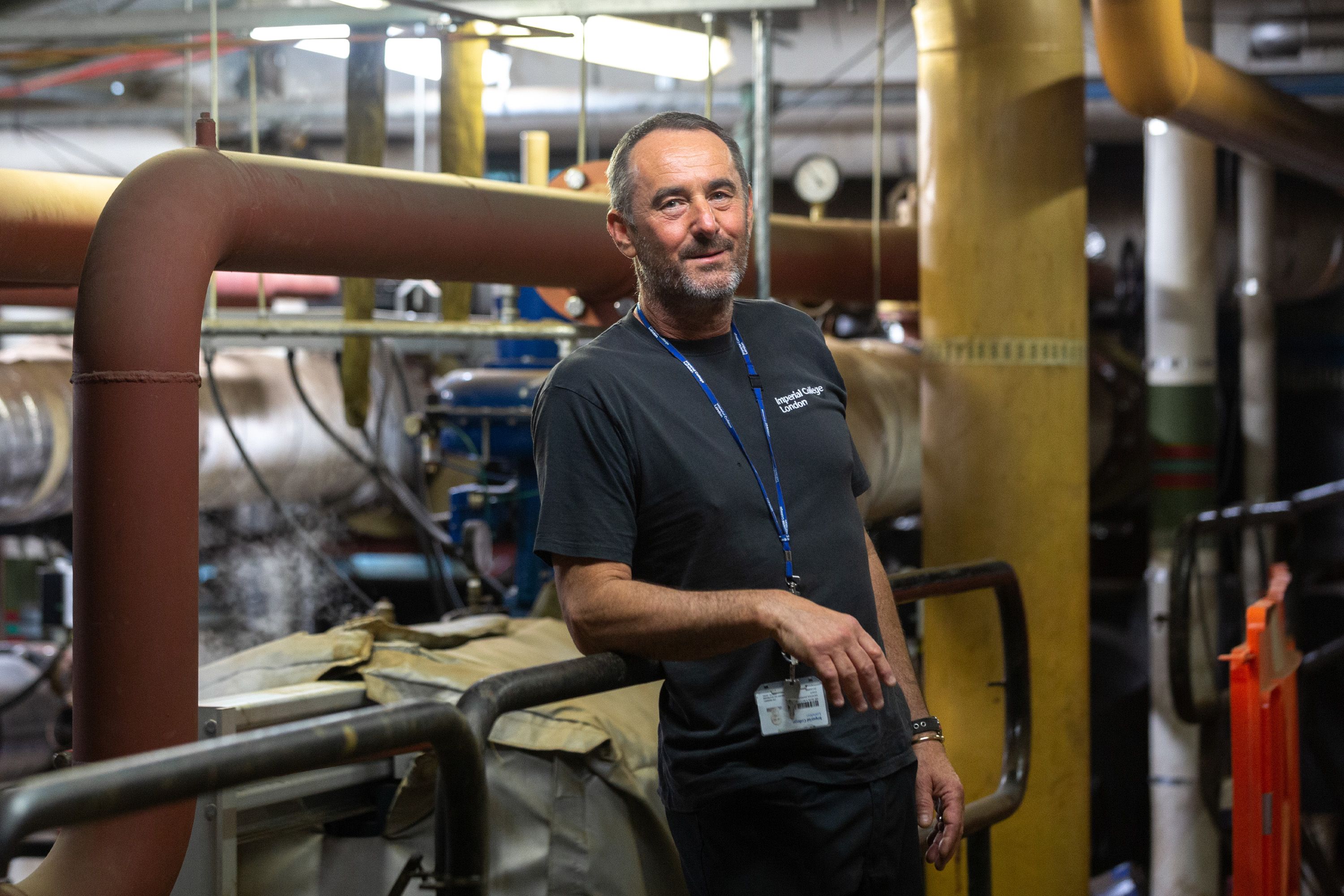 A man in a blue Imperial T-shirt stands among pipes and boilers